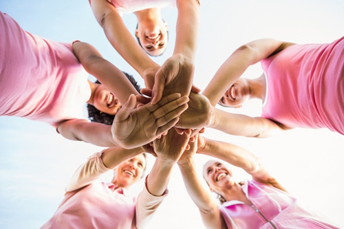 Grupo de mujeres con las manos unidas vestidas de rosa contra el cáncer de mama